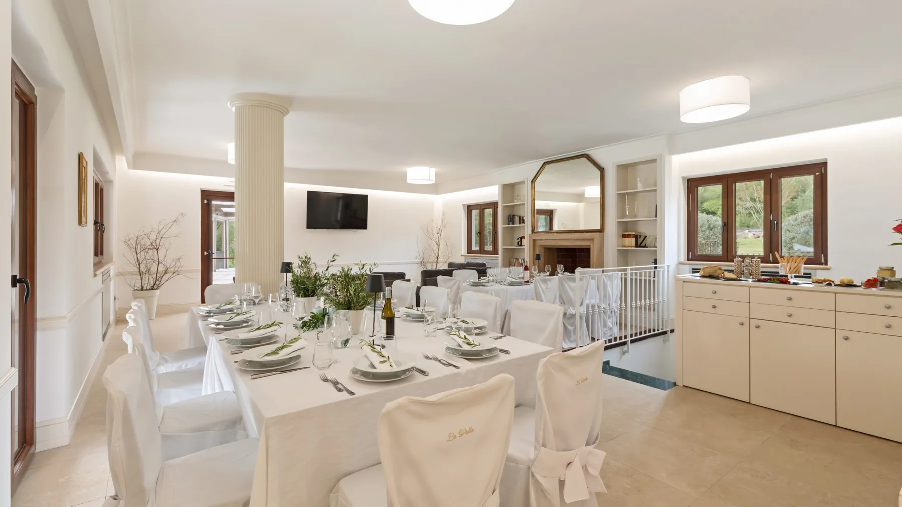 A bright dining room with a long set table and a kitchen along the wall.