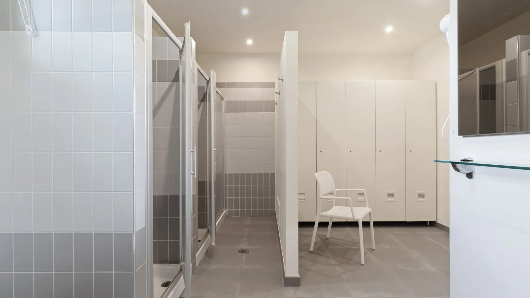 A tiled bathroom area with shower stalls and white storage cabinets.