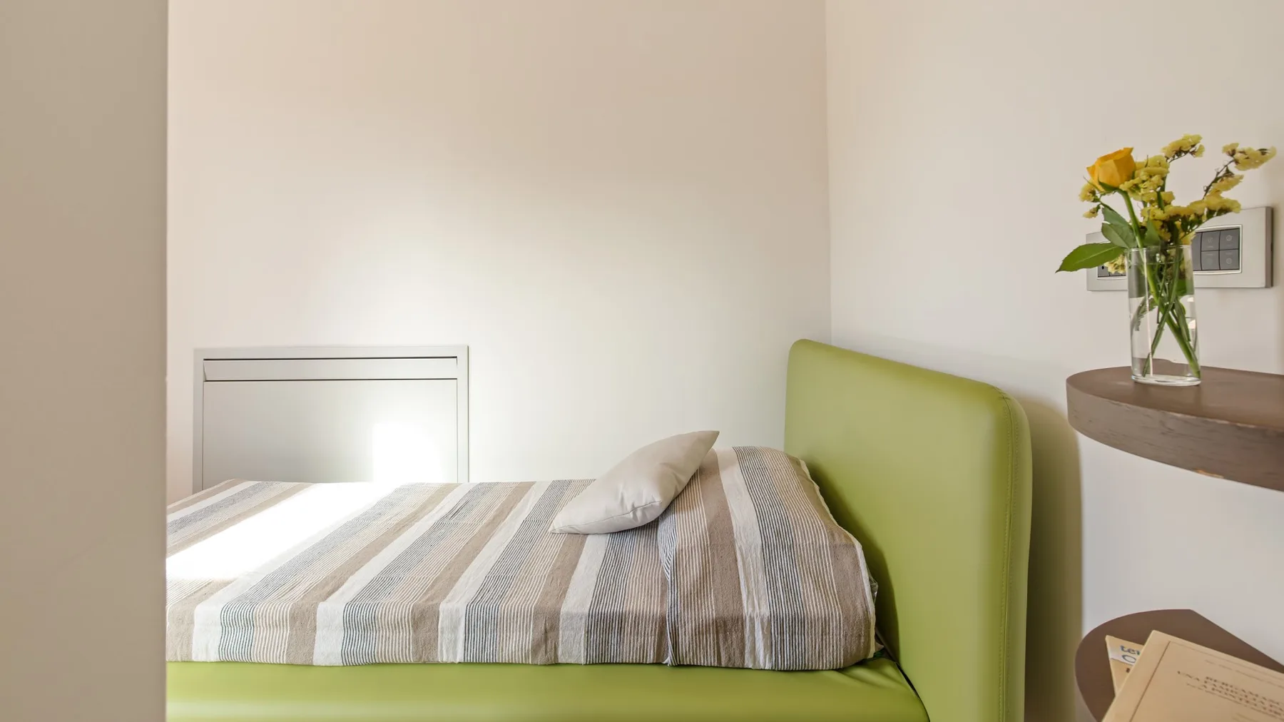 A bedroom with a single bed, striped bedding, and a green headboard.