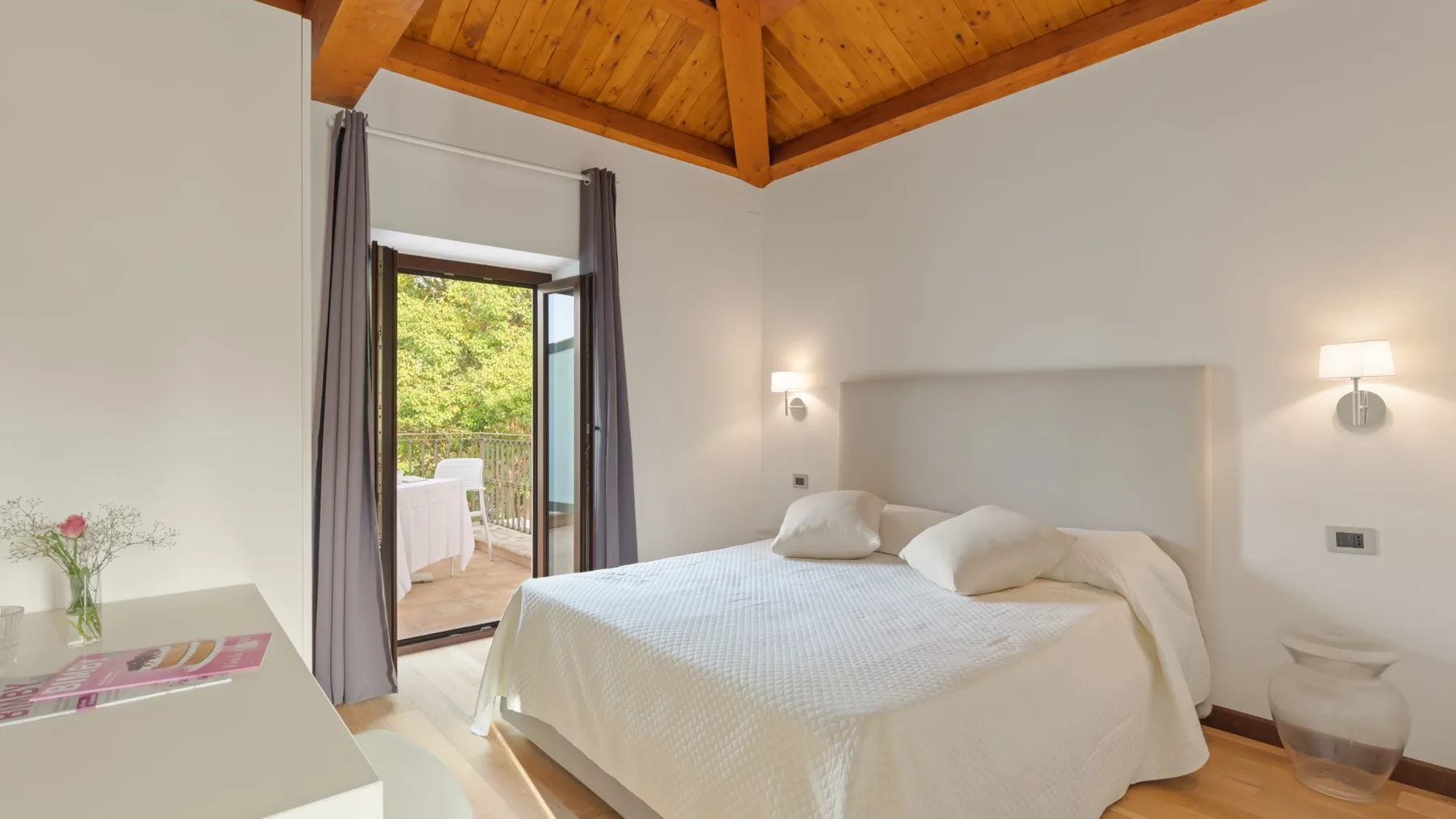 A bright bedroom with a neatly made bed beneath a timber ceiling.