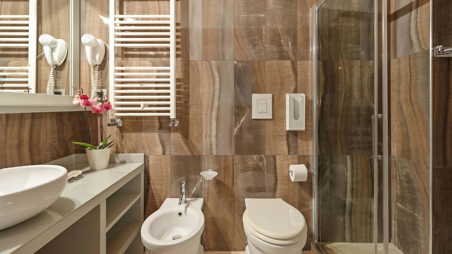 A tiled bathroom with a sink, toilet, bidet, and glass shower.