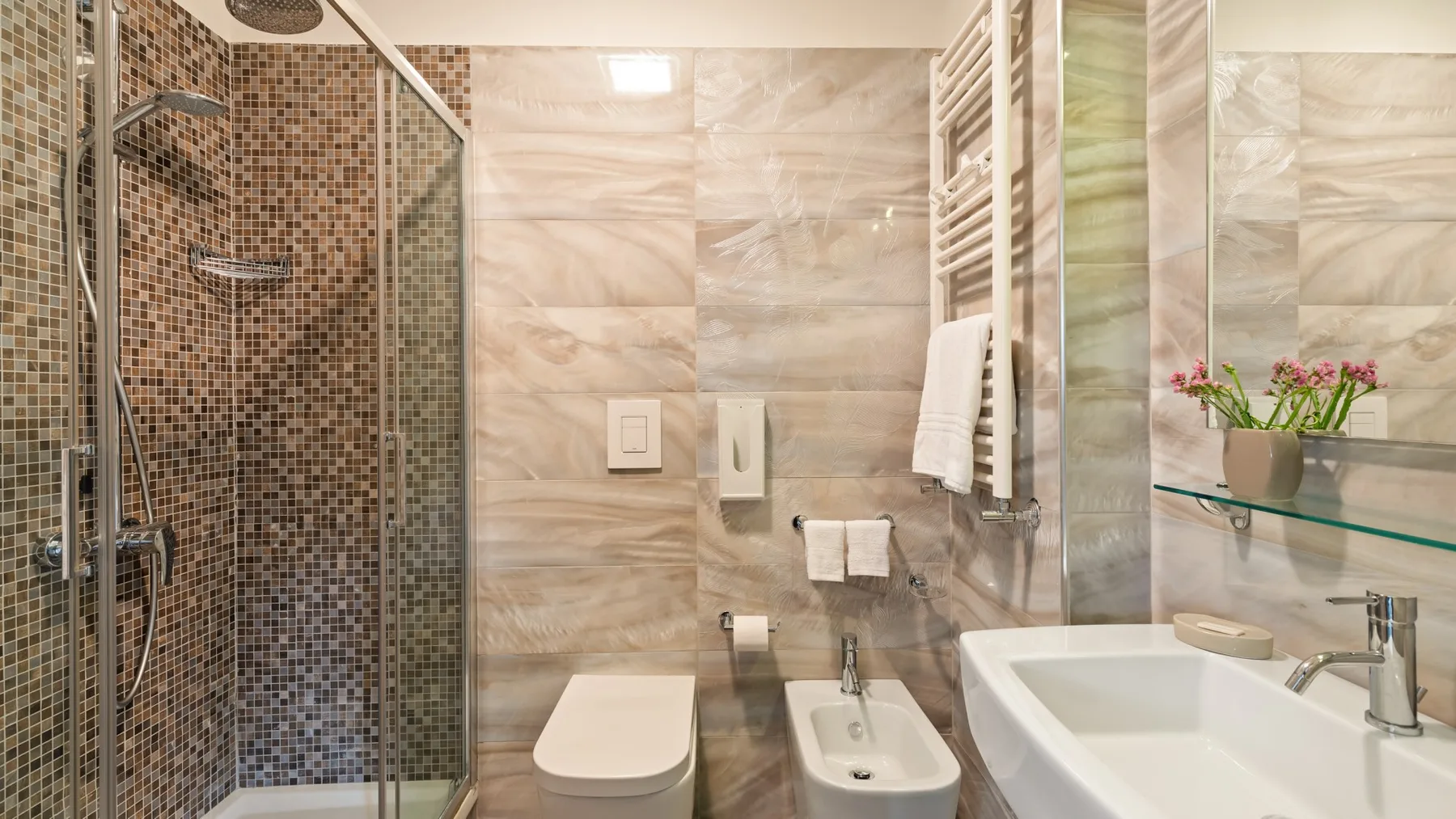 A bathroom with a glass shower, toilet, bidet, and sink.