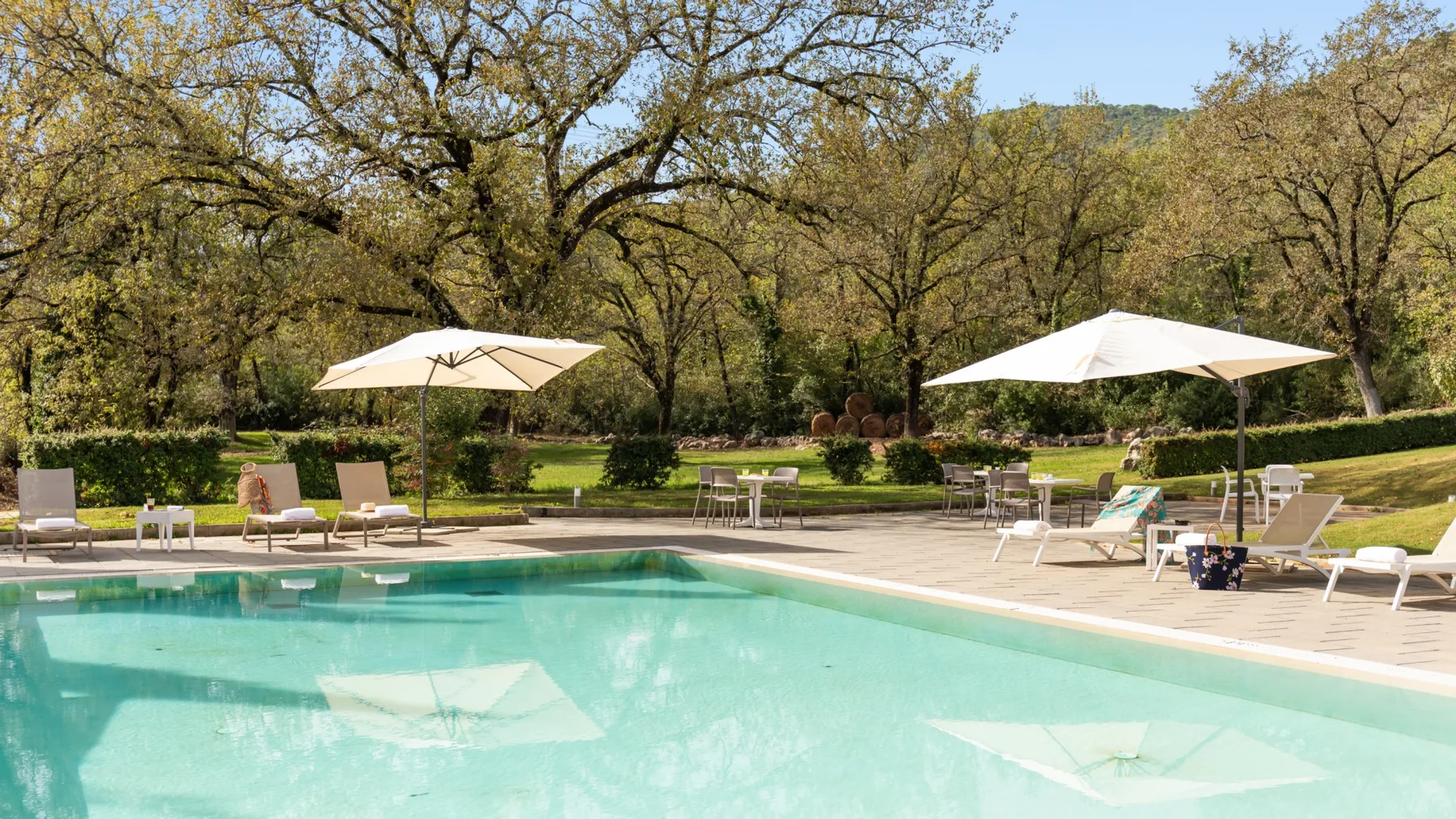 An outdoor swimming pool is surrounded by lounge seating and open umbrellas.