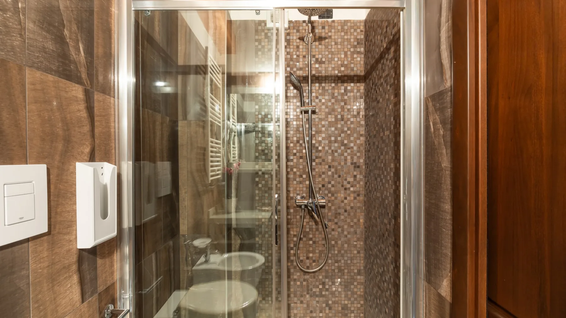 A tiled bathroom shower with a handheld showerhead and glass panels.