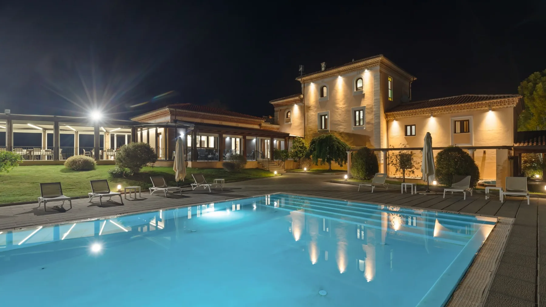 An illuminated outdoor swimming pool in front of a large building at night.