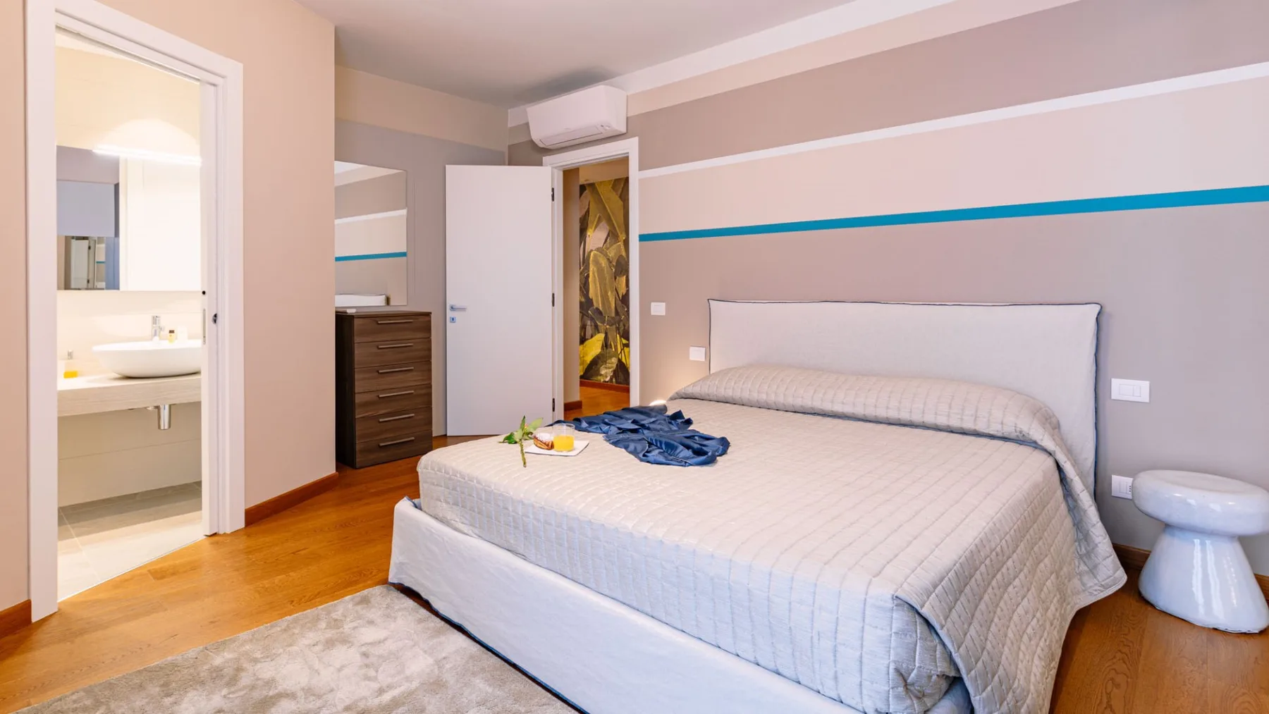 Un dormitorio con la cama tendida y una puerta abierta hacia el baño.