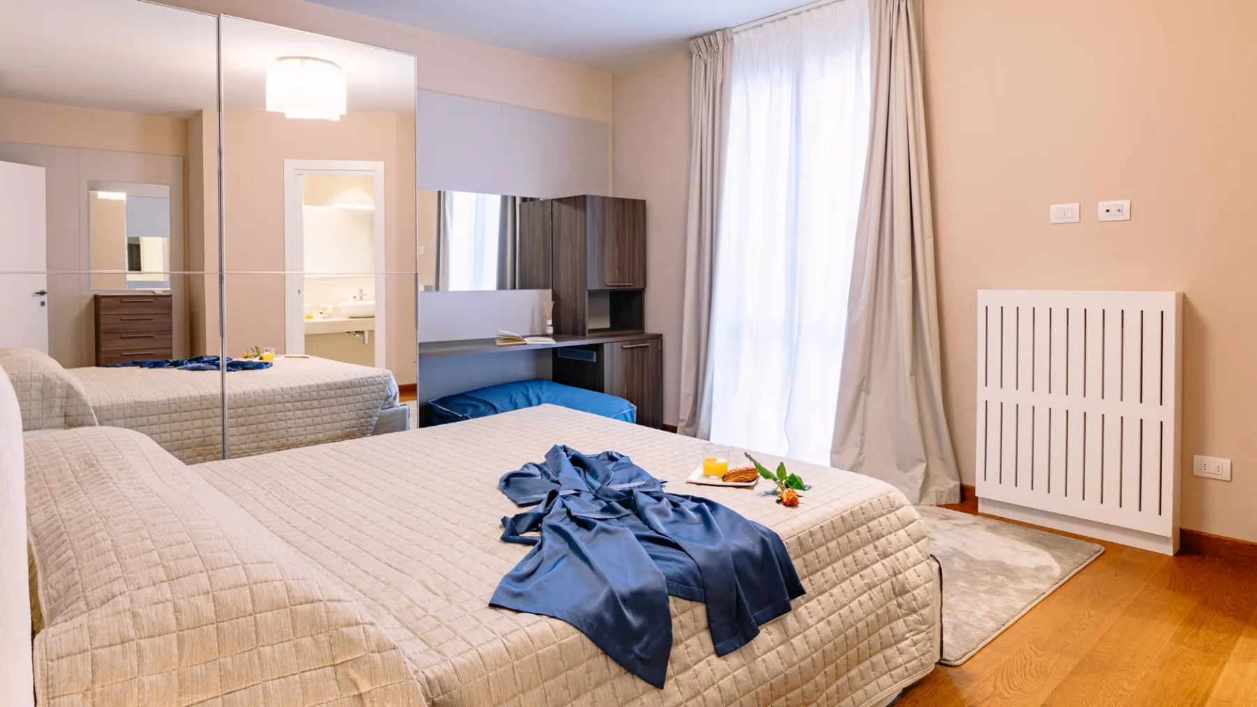 Un dormitorio con una cama grande, un armario con espejo y una ventana luminosa con cortinas.