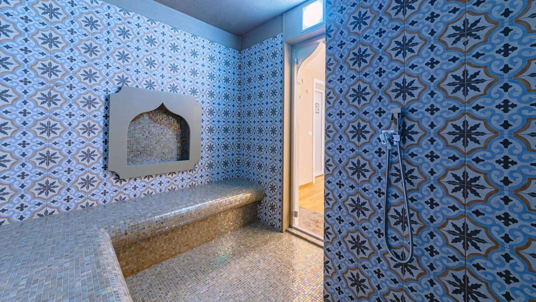 Un baño revestido de azulejos cuenta con un banco integrado y una ducha en la pared.