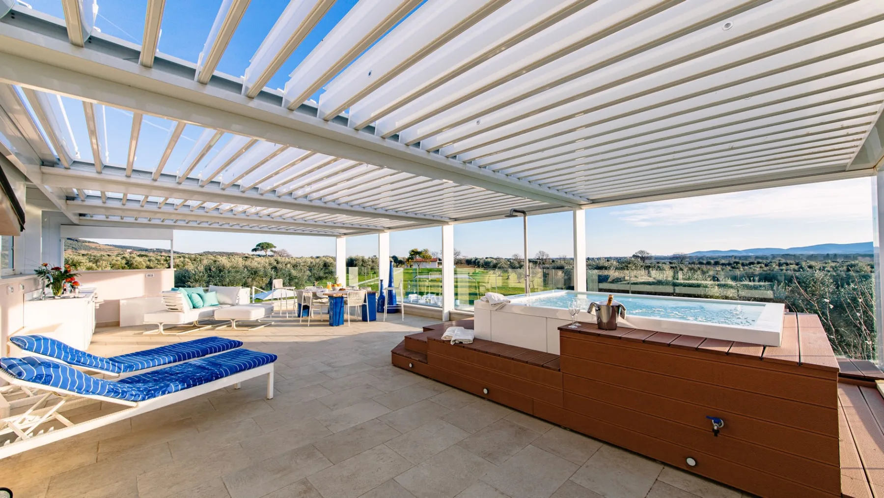 Una terraza exterior cubierta tiene asientos, una tumbona y una bañera de hidromasaje.