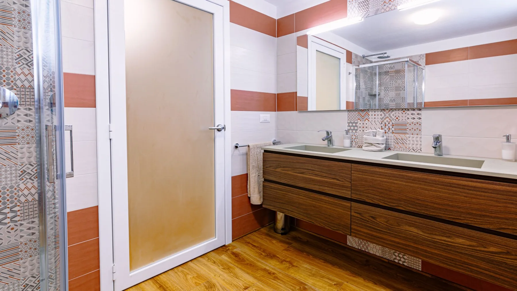 Un baño alicatado con un mueble de lavabo largo, espejo y ducha de vidrio.