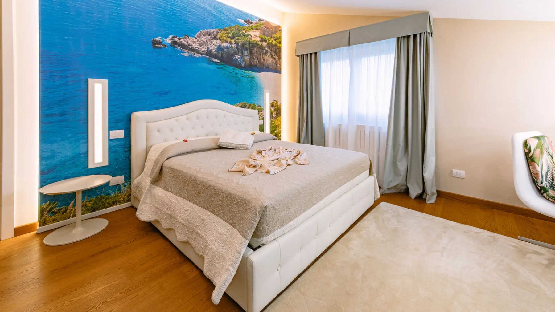 Un dormitorio con una cama, un mural costero y una ventana con cortinas.