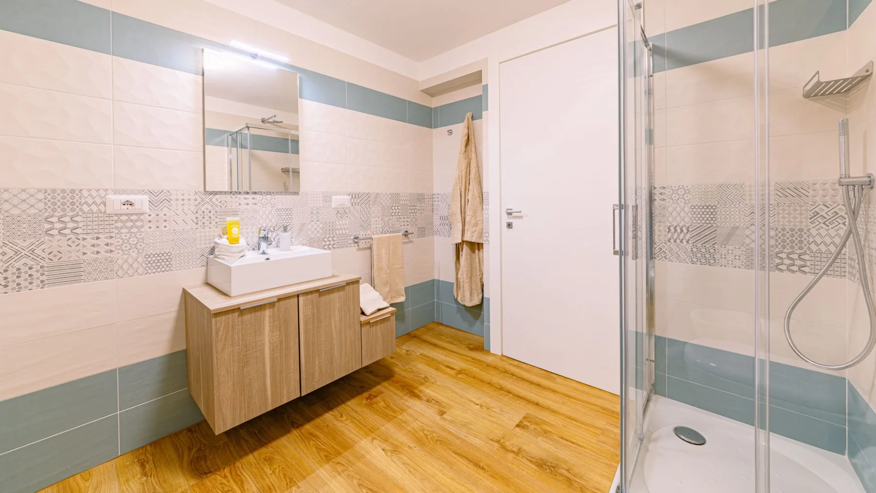 Un baño luminoso con lavabo, espejo de pared y ducha de cristal.