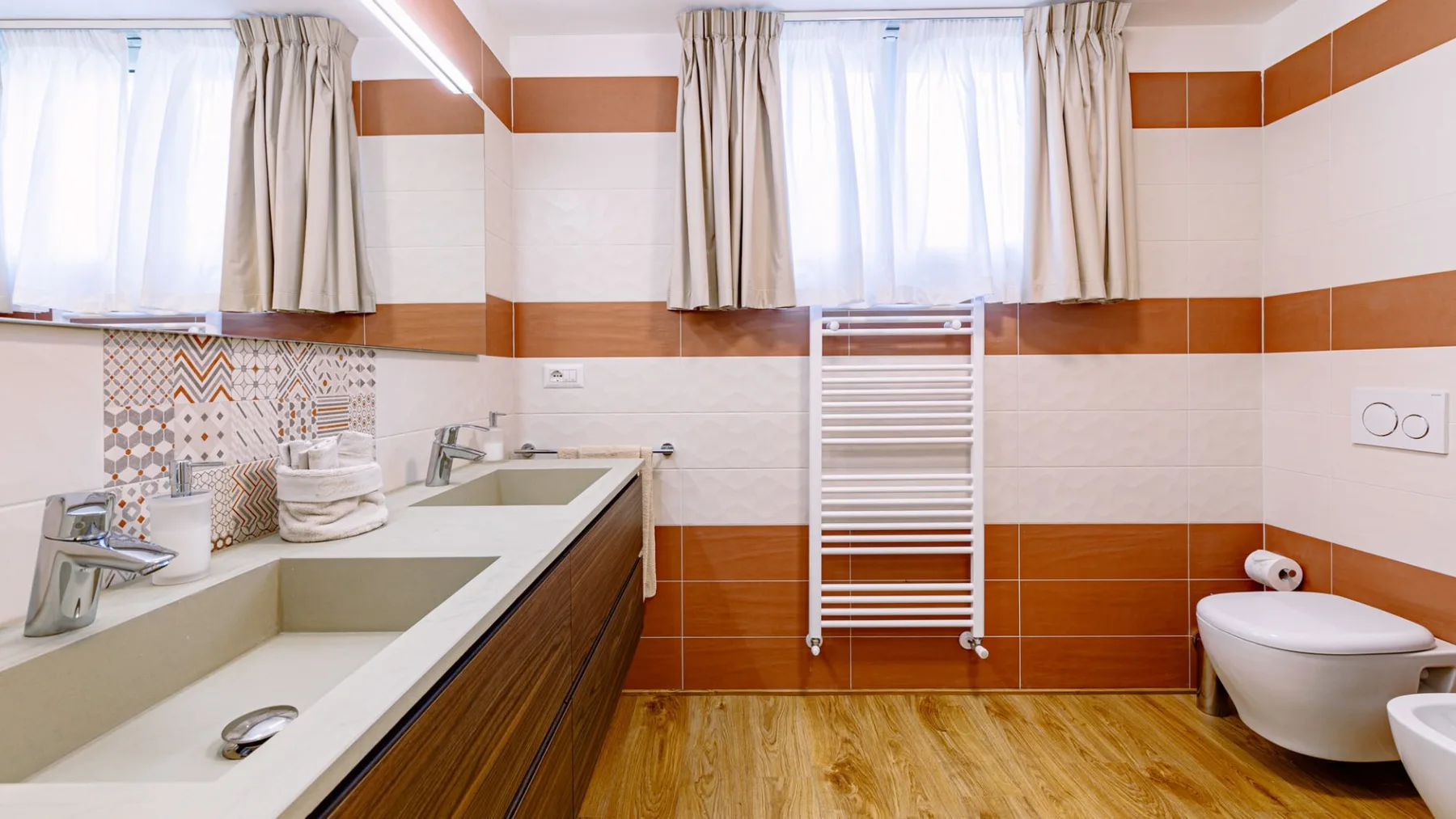 Un baño alicatado con bañera, inodoro y ventanas luminosas con cortinas.