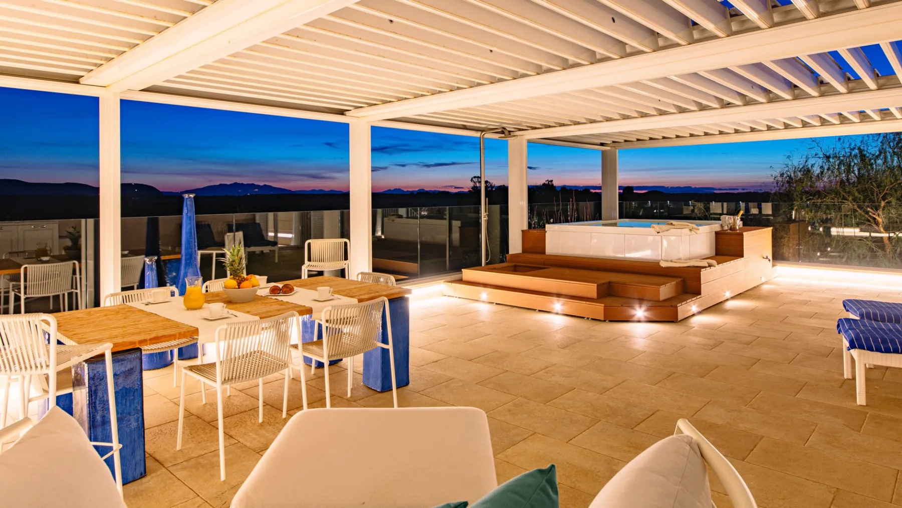 Una terraza exterior cubierta con mesas de comedor y una zona de estar al anochecer.
