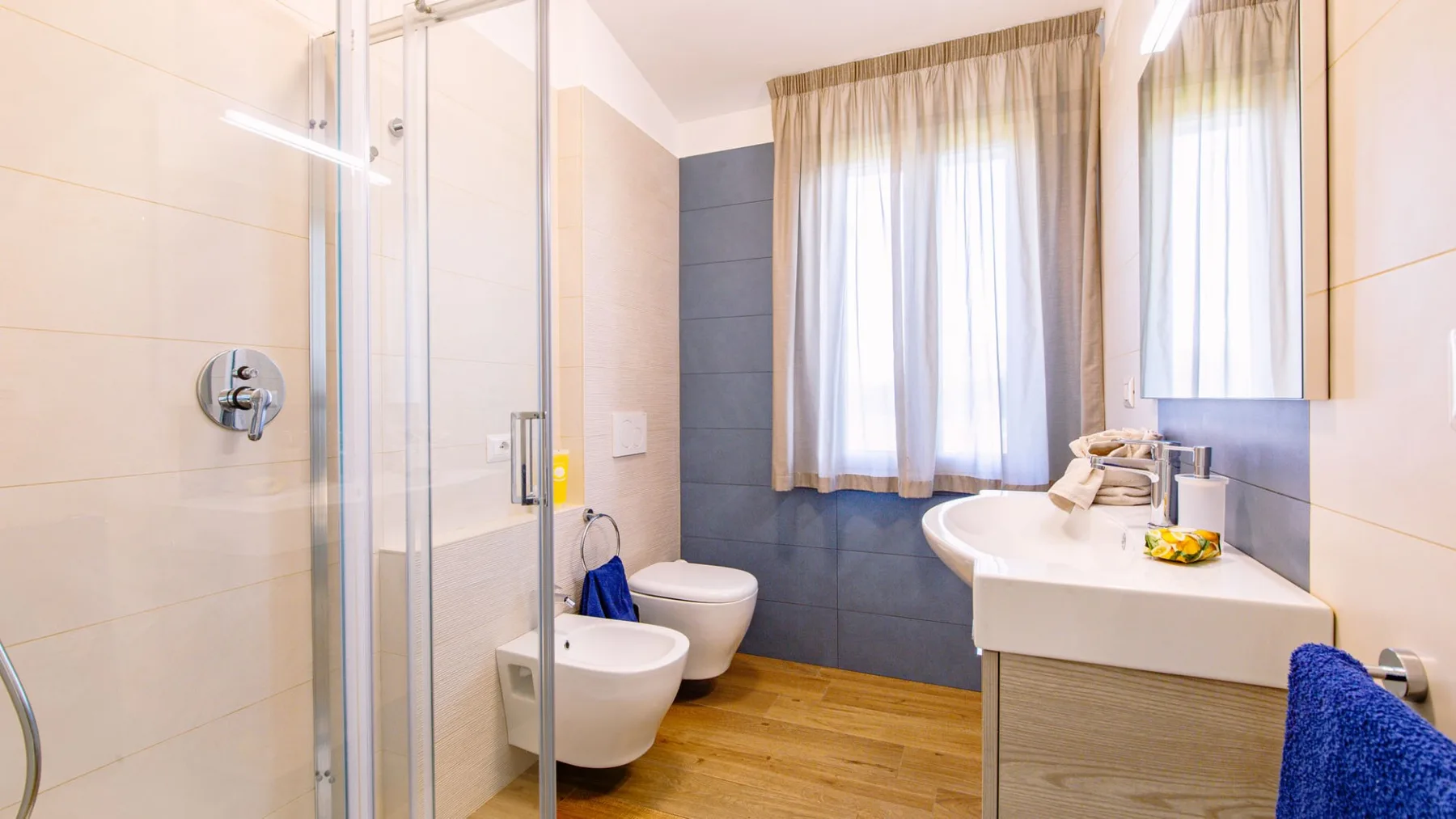 Un baño luminoso con ducha de vidrio, inodoro y lavabo bajo una ventana.