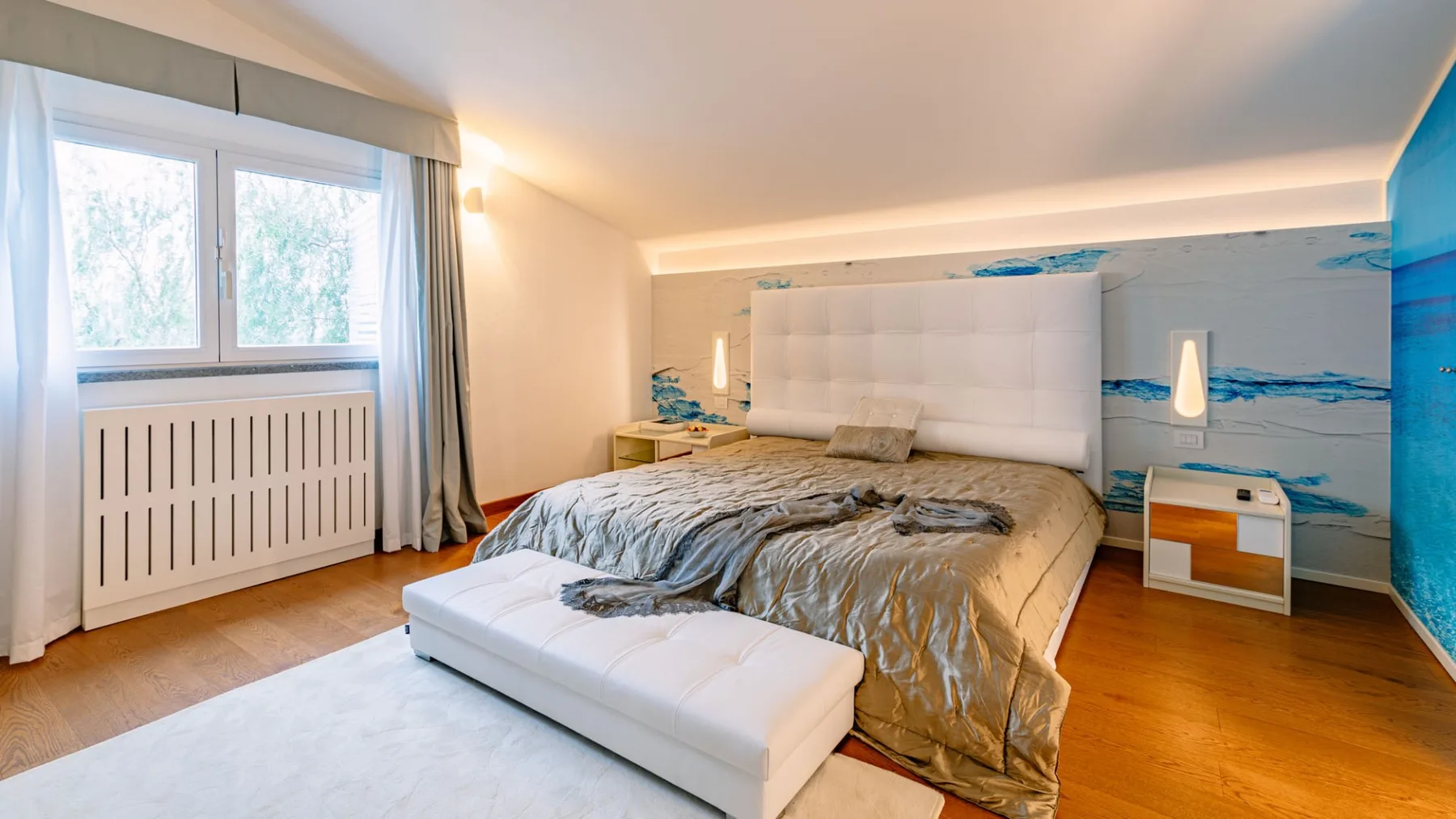 Un dormitorio con una cama grande, cabecero blanco tapizado y ventanas.
