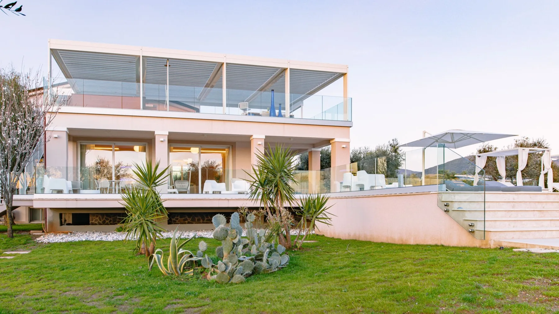Una casa moderna con una terraza superior con barandilla de vidrio da a un césped verde.