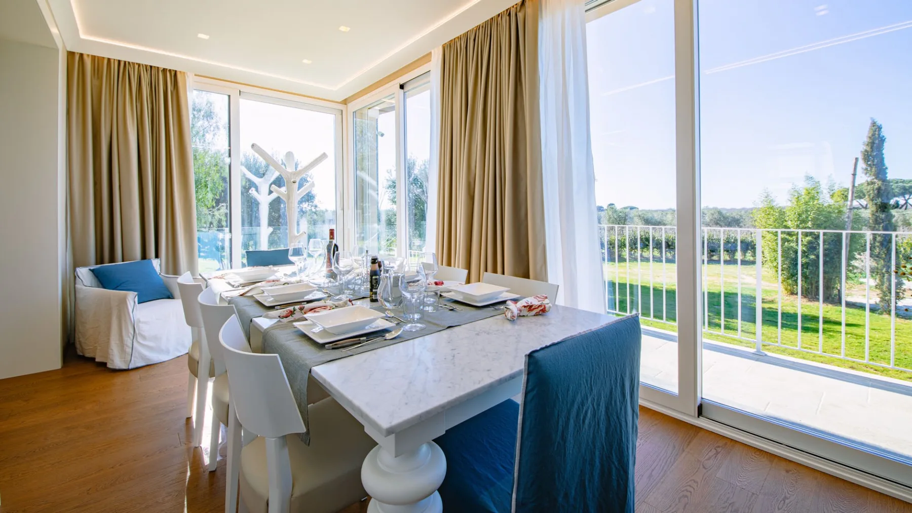 Un comedor luminoso con una mesa puesta junto a grandes ventanales que dan a un balcón.