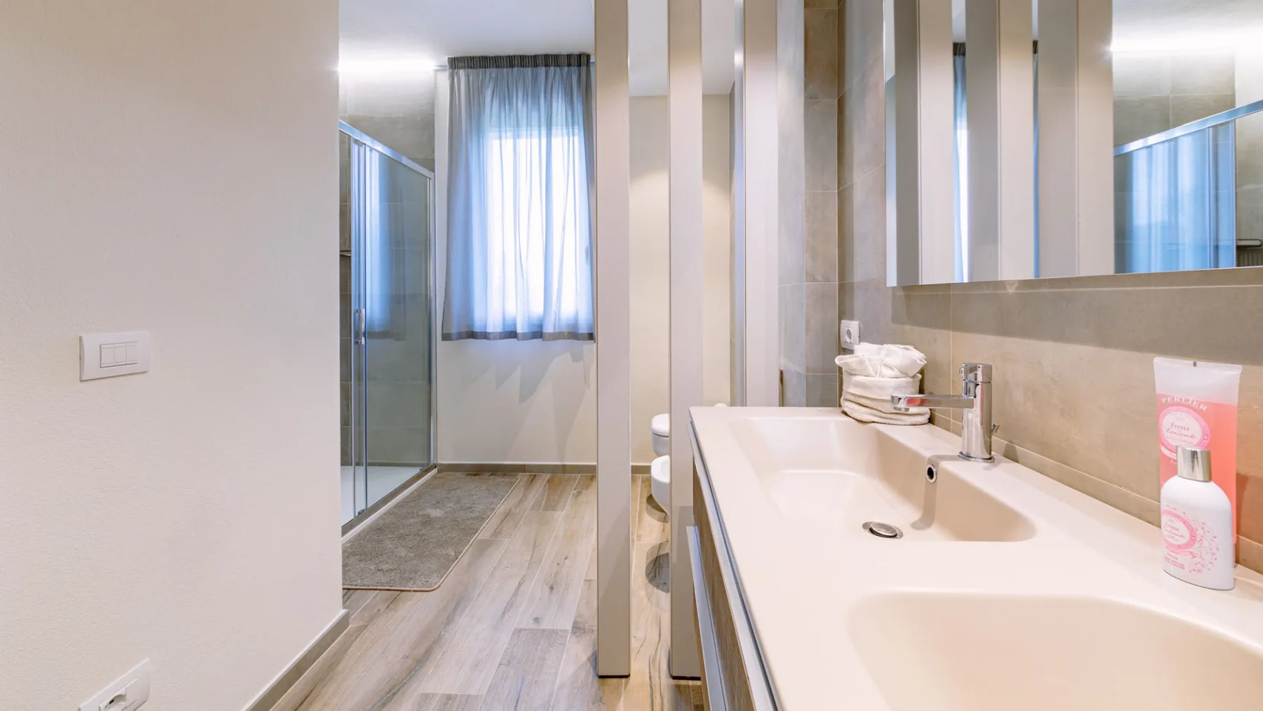 Un baño luminoso tiene una encimera larga con lavabo junto a una ducha de vidrio.