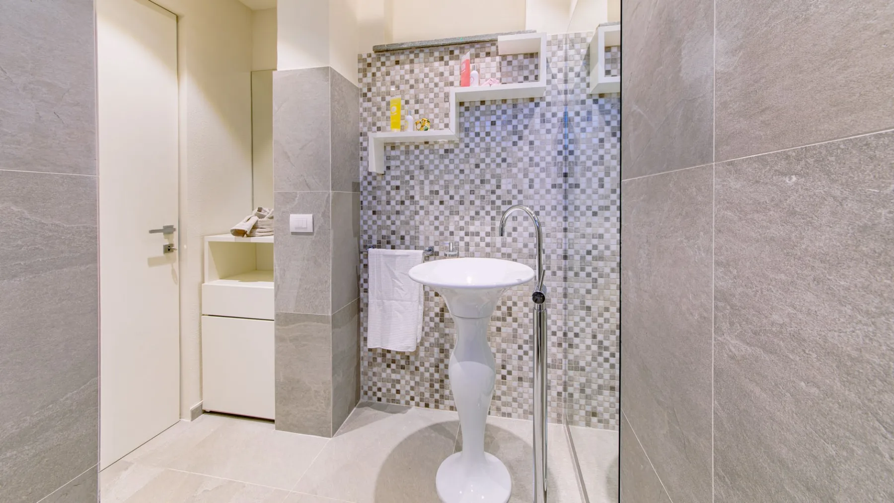 Un baño alicatado con un lavabo de pedestal y un estante en la pared.