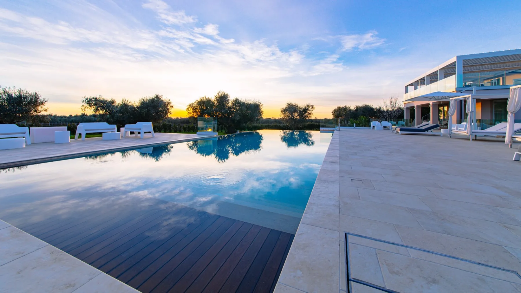 Una piscina al aire libre junto a un edificio moderno, con una amplia terraza pavimentada.