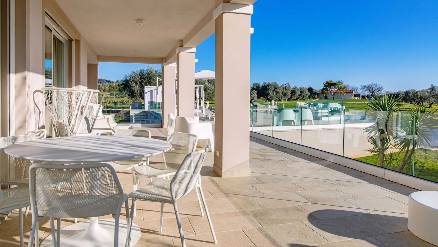 Una terraza exterior cubierta con asientos de comedor da a una piscina.