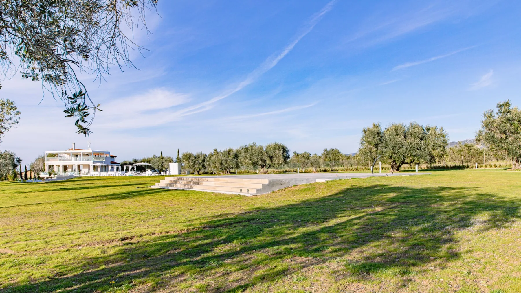 Una amplia zona de césped al aire libre, con árboles y un edificio bajo a lo lejos.