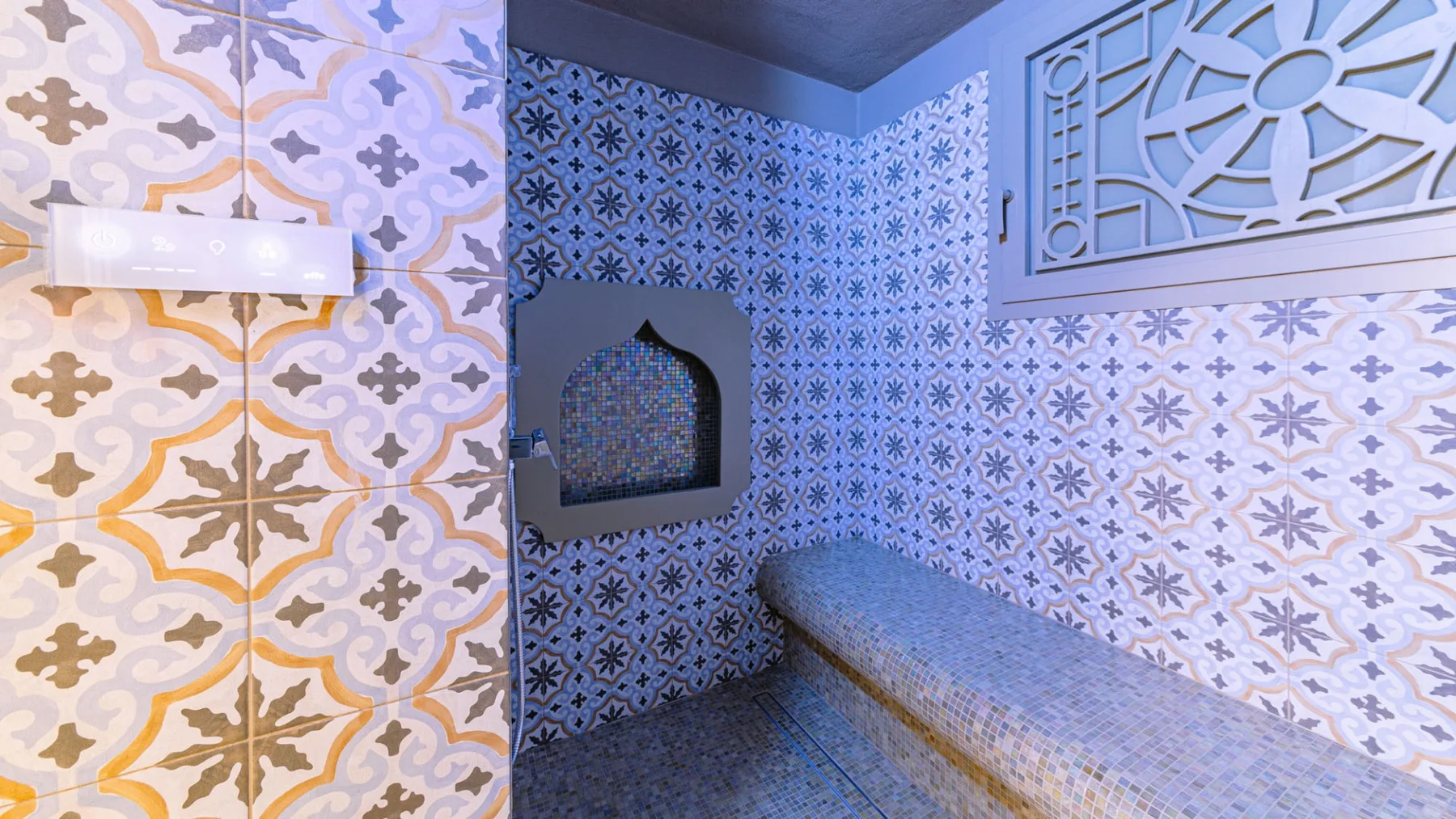 Un baño alicatado con un banco integrado y diseños decorativos en las paredes.