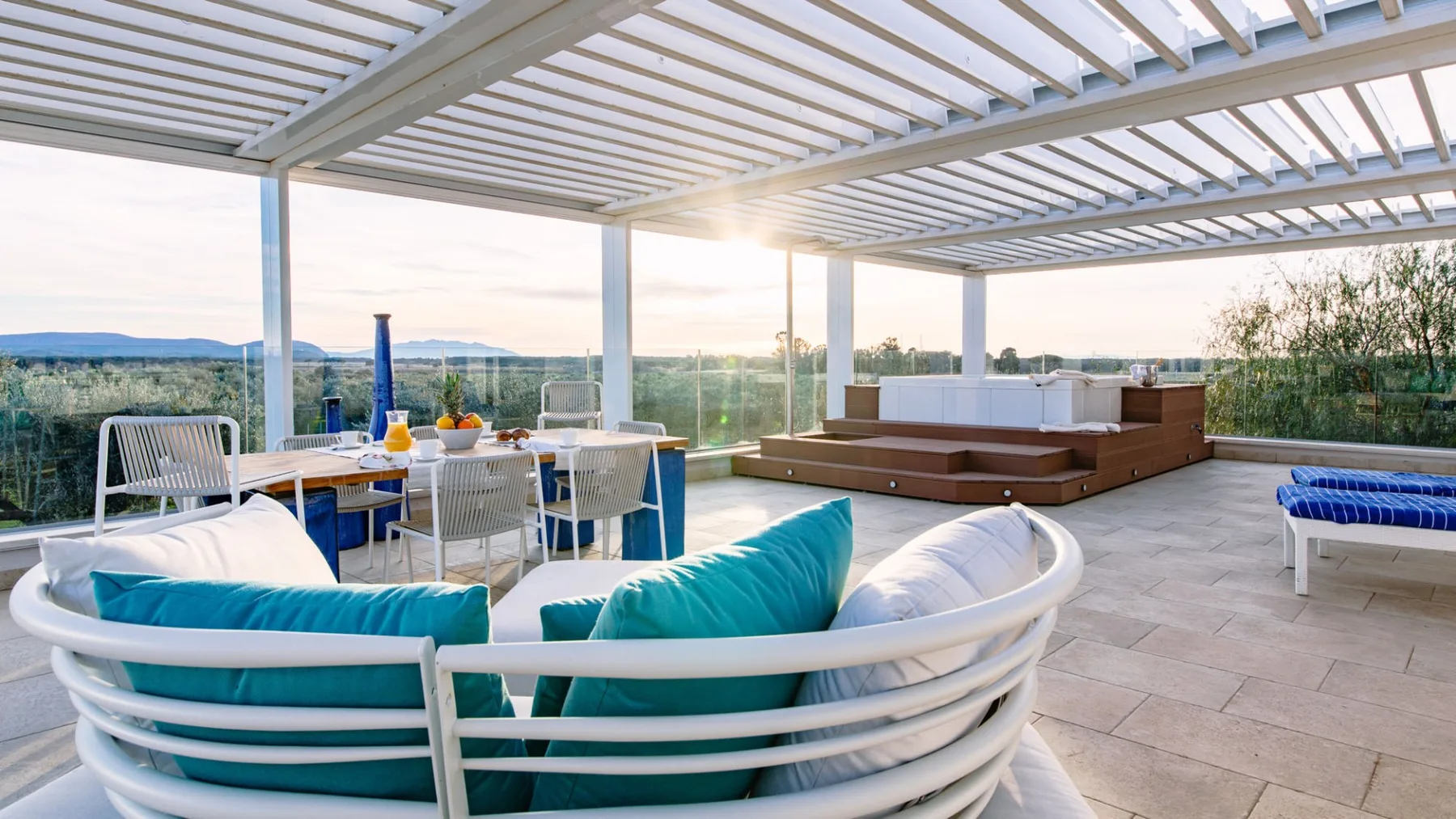 Una terraza en la azotea tiene asientos curvos, una mesa de comedor y una bañera de hidromasaje elevada bajo una pérgola.