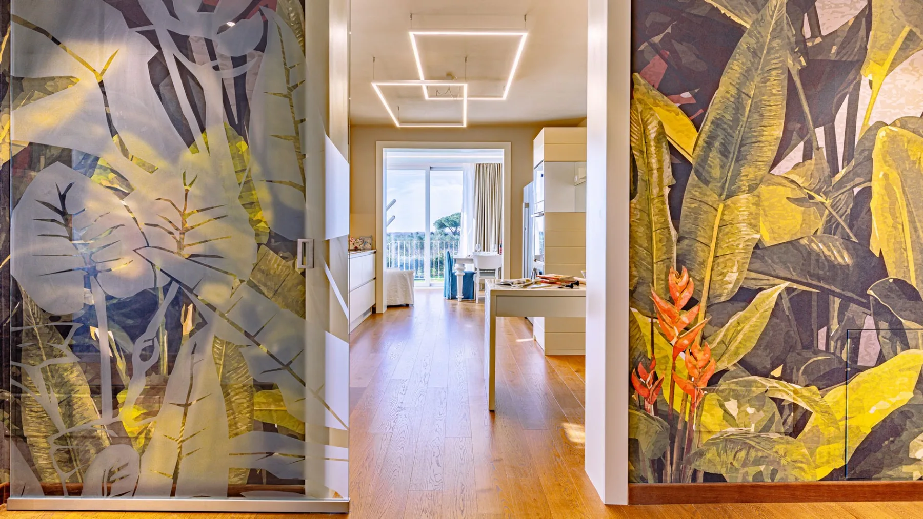 Una habitación luminosa con un pasillo central, puertas de vidrio y grandes murales botánicos.