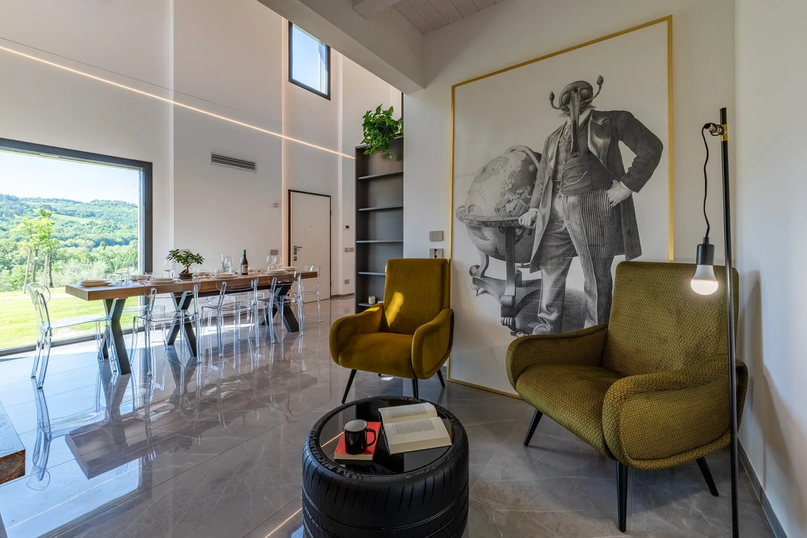 Una luminosa zona de comedor y estar cuenta con una mesa larga, dos sillones y una gran obra enmarcada.