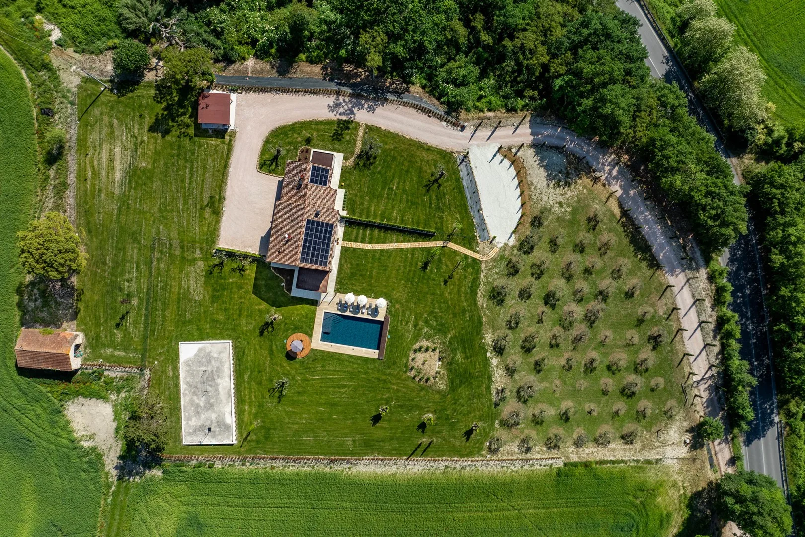Vista aérea de una casa, una piscina y céspedes junto a un huerto y una entrada curva.