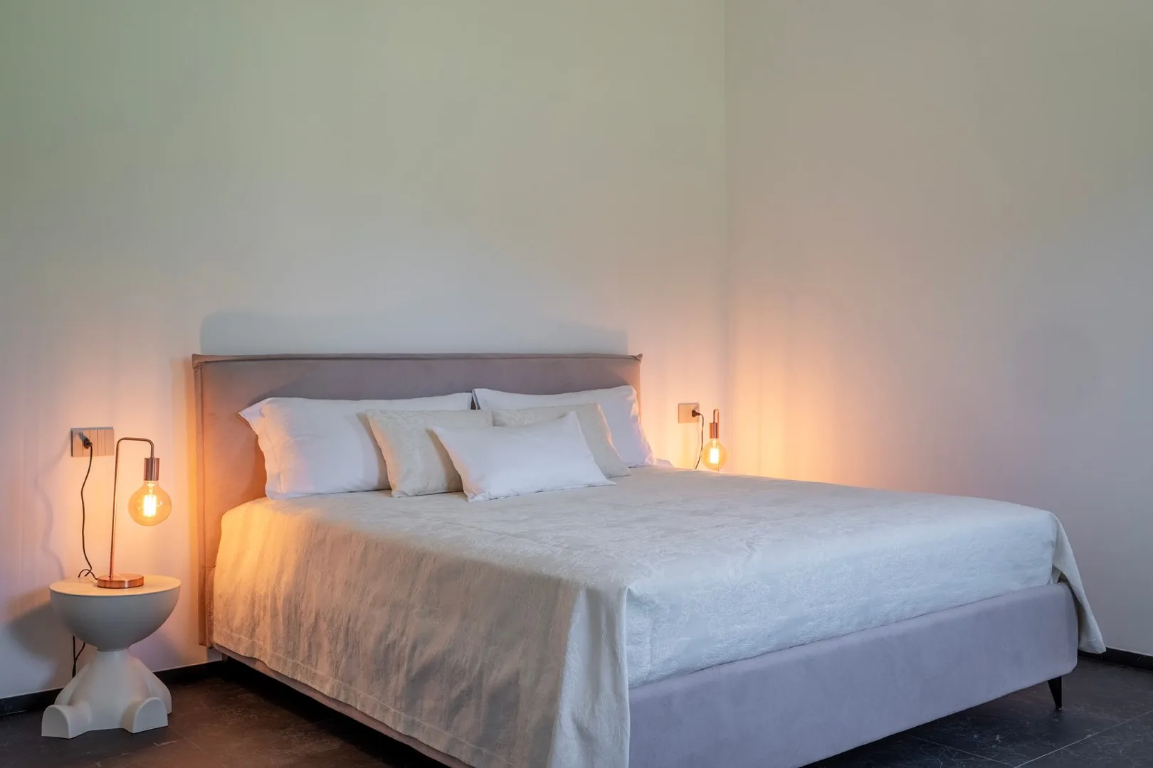 Un dormitorio con una cama bien tendida, ropa de cama blanca y luces cálidas junto a la cama.