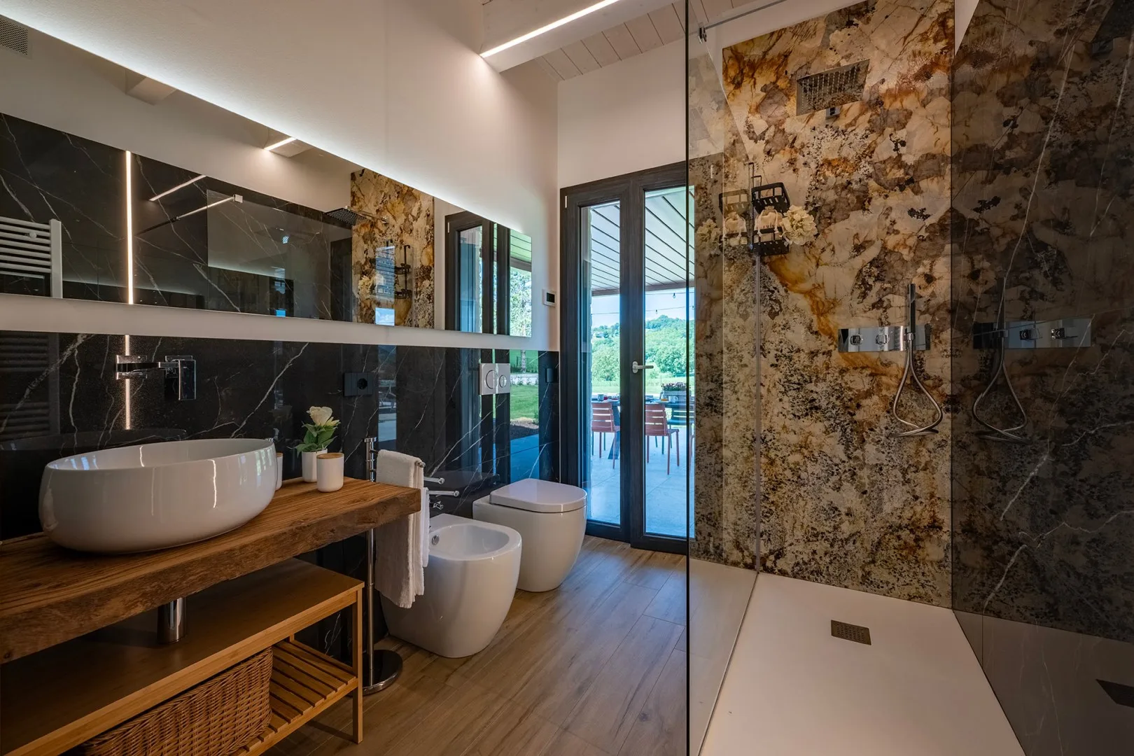 Un baño moderno cuenta con un mueble de madera, lavabo sobre encimera, inodoro y ducha a ras de suelo con mampara.