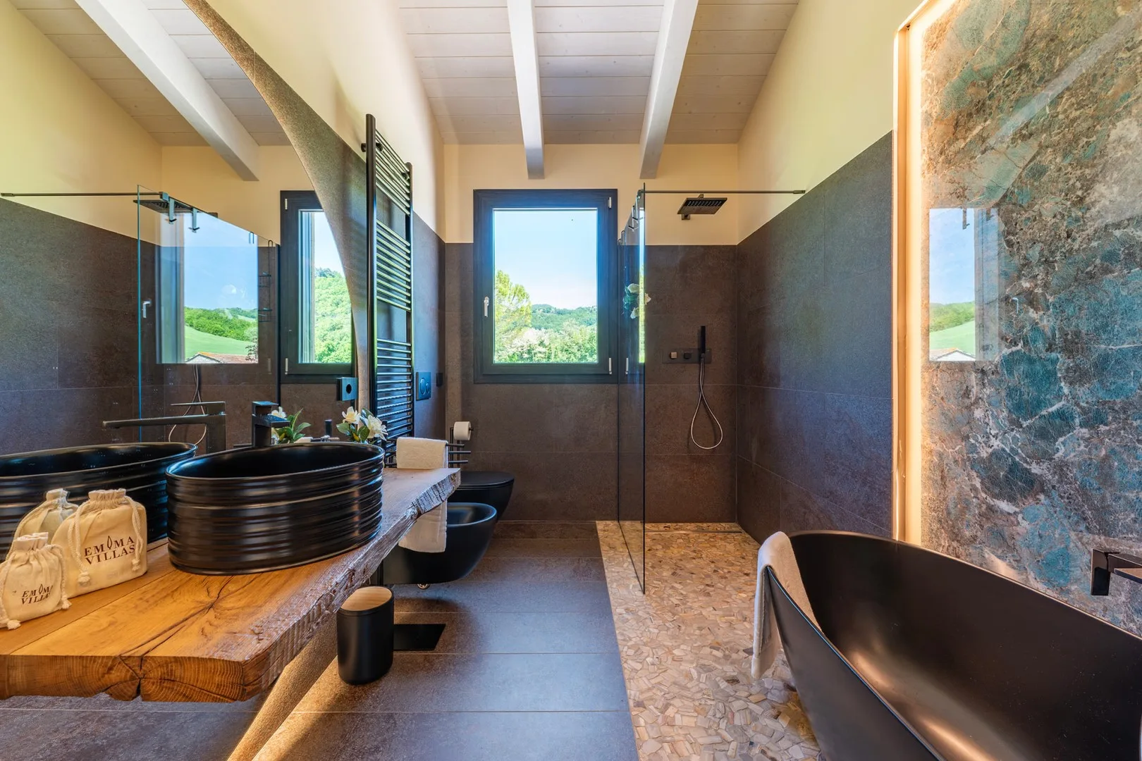 Un baño amplio con encimera de madera, lavabos negros sobrepuestos, ducha a ras de suelo y bañera independiente.