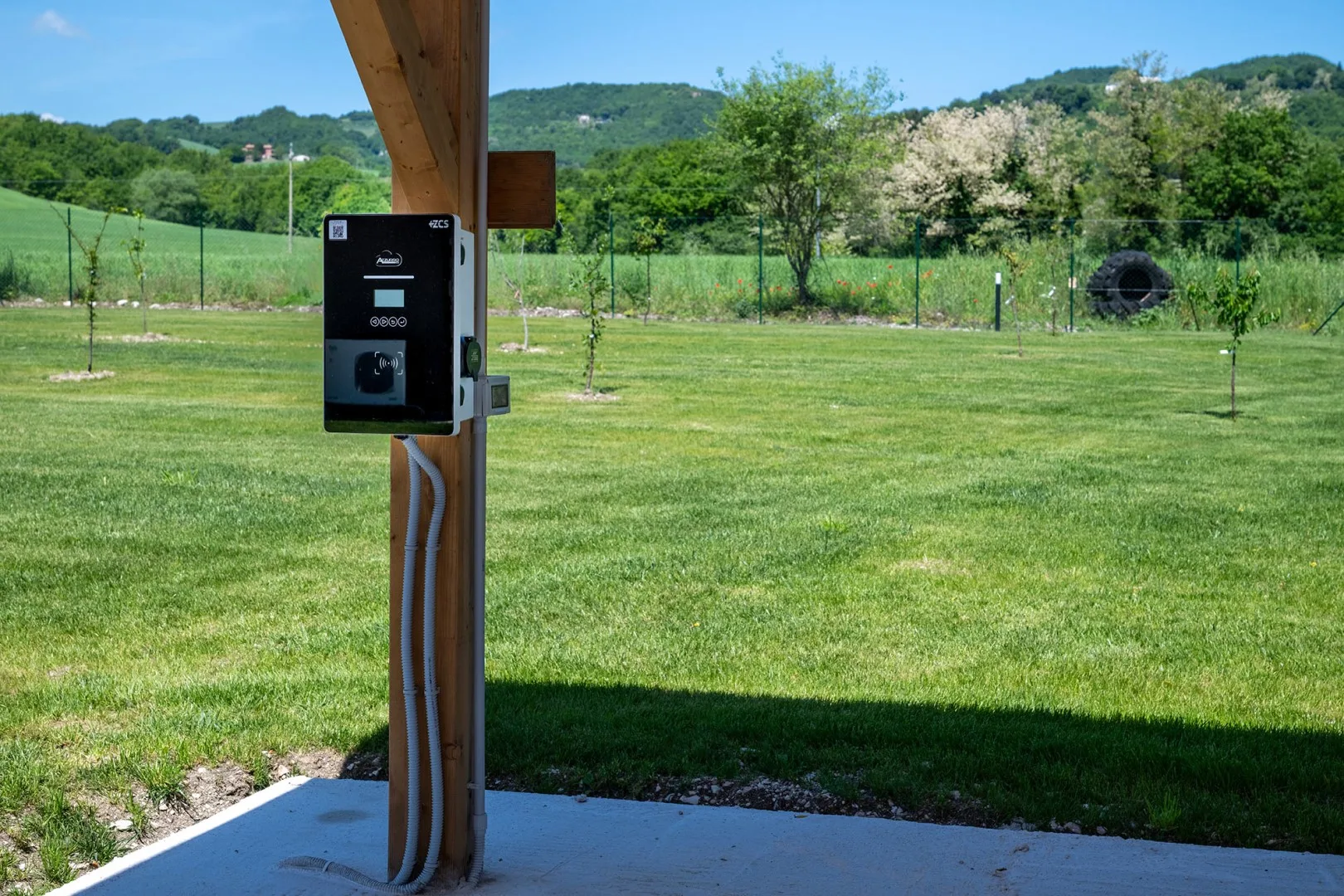 Un campo de hierba al aire libre, con un panel de control negro en un poste de madera y colinas arboladas al fondo.