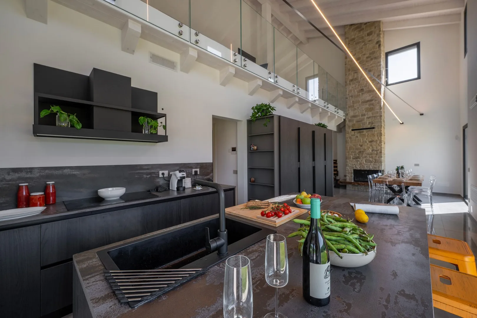 Una cocina moderna y amplia cuenta con una isla oscura, verduras y una alta pared de piedra.