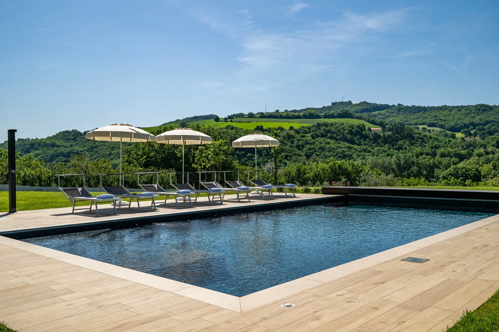 Una piscina al aire libre está rodeada por una terraza de madera, tumbonas y sombrillas.