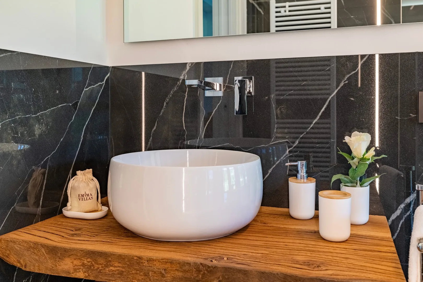 Un lavabo blanco sobre una encimera de madera destaca frente a una pared de baño oscura con vetas de mármol.