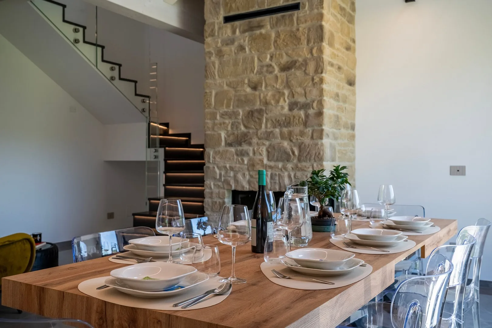 Una mesa de comedor está puesta con platos y copas junto a una columna de piedra y una escalera.
