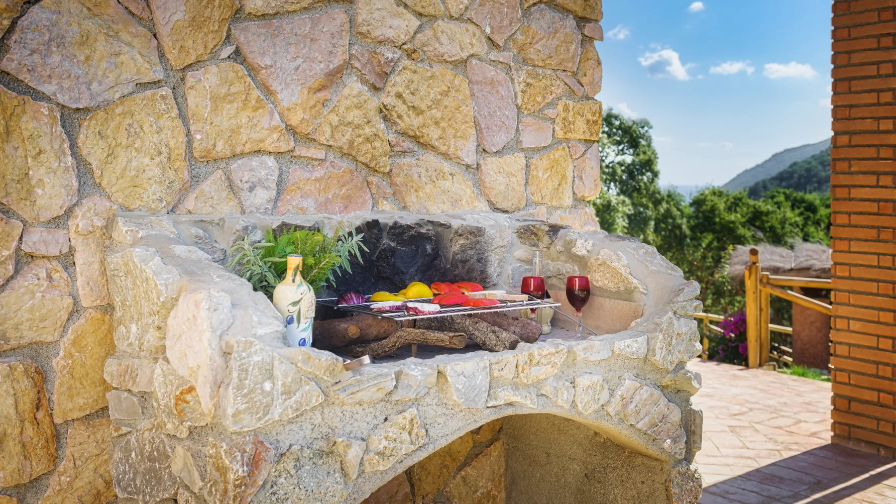 Una zona de barbacoa de piedra al aire libre con comida y bebidas sobre la parrilla.
