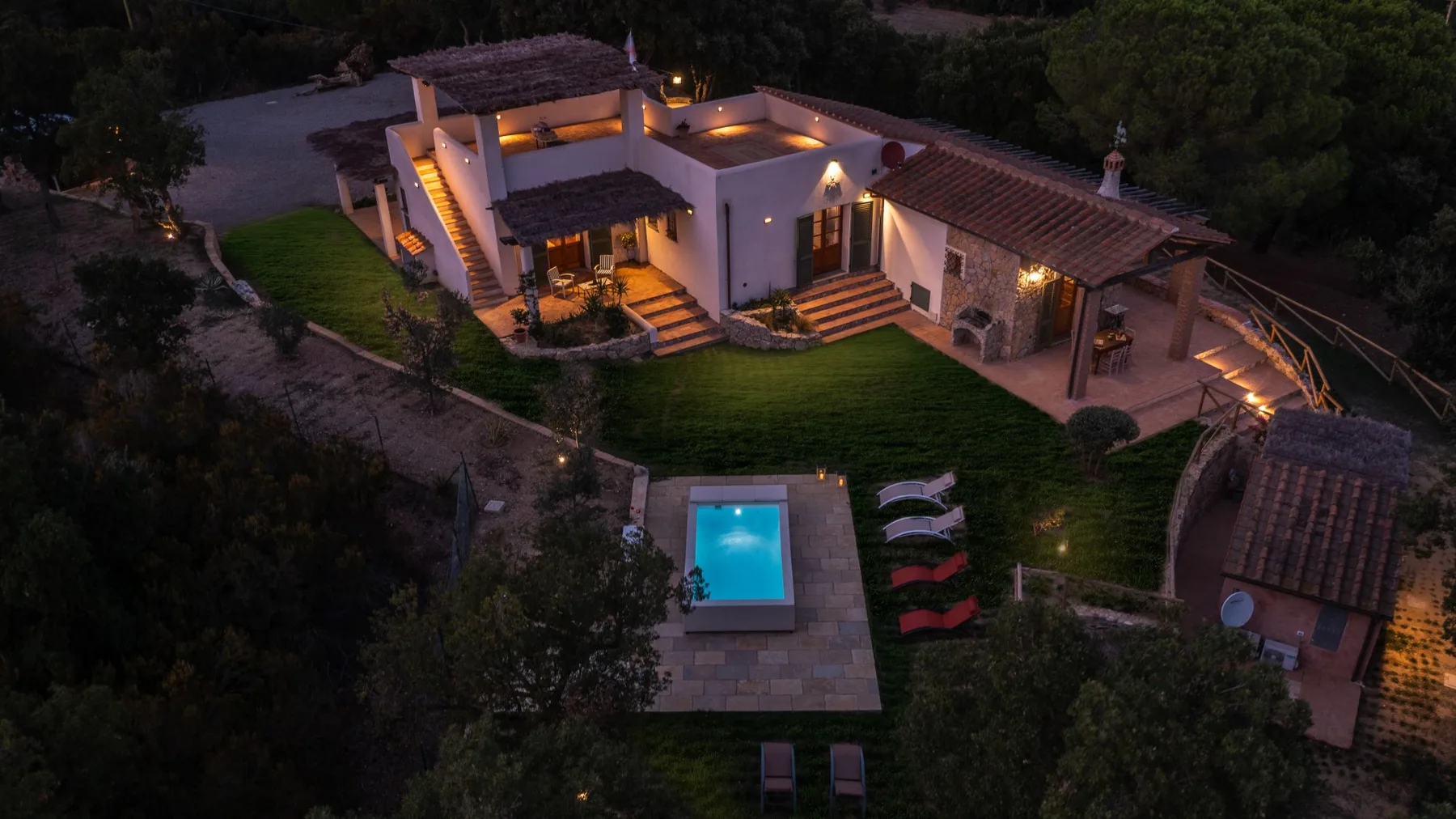Una casa iluminada y una piscina están junto a un jardín al anochecer.