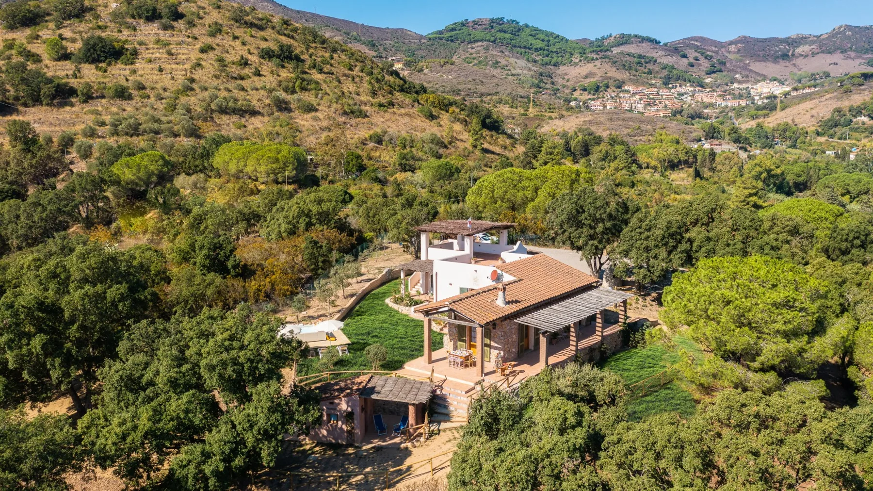 Una casa está entre árboles en una ladera verde, con montañas a lo lejos.