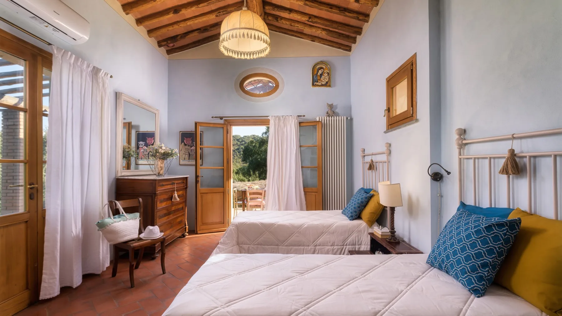 Un dormitorio luminoso con dos camas, vigas de madera en el techo y una puerta abierta hacia la vegetación.