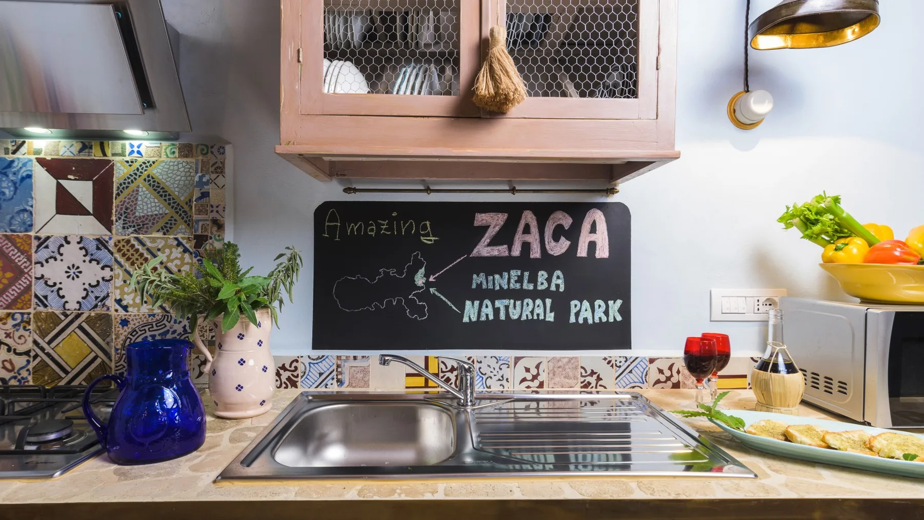 Una encimera de cocina con fregadero, azulejos estampados y una pizarra.
