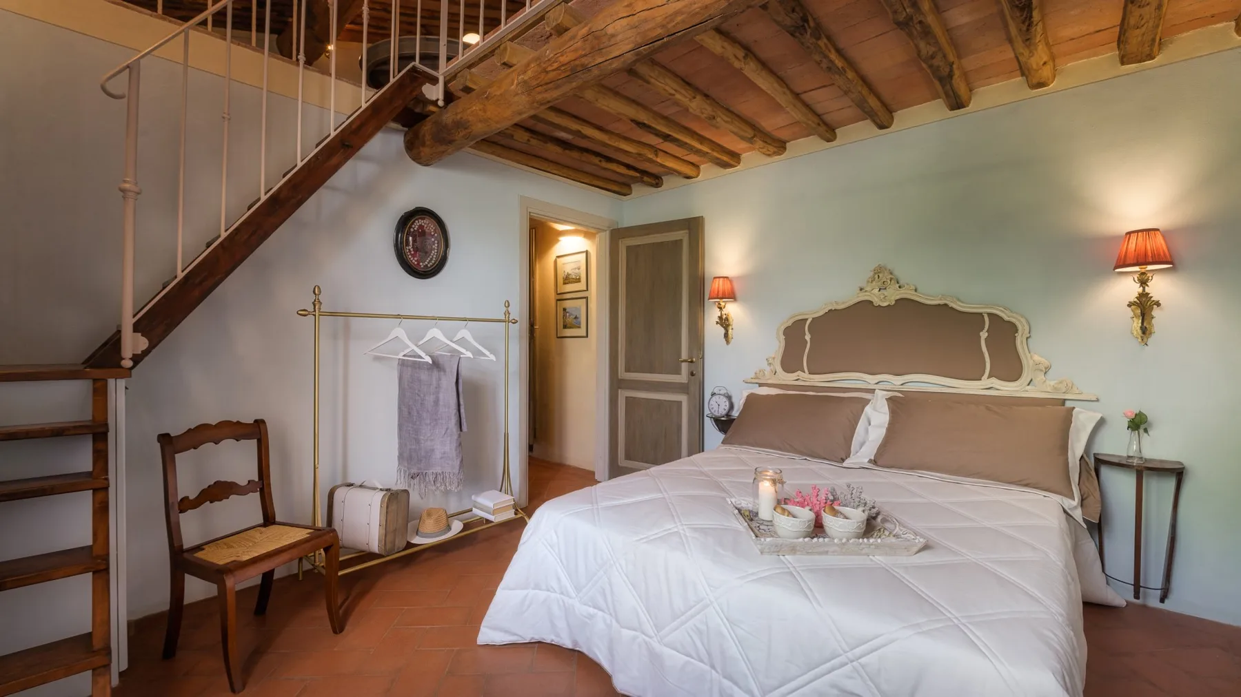 Un dormitorio con una cama grande bajo vigas de madera vistas y una escalera.