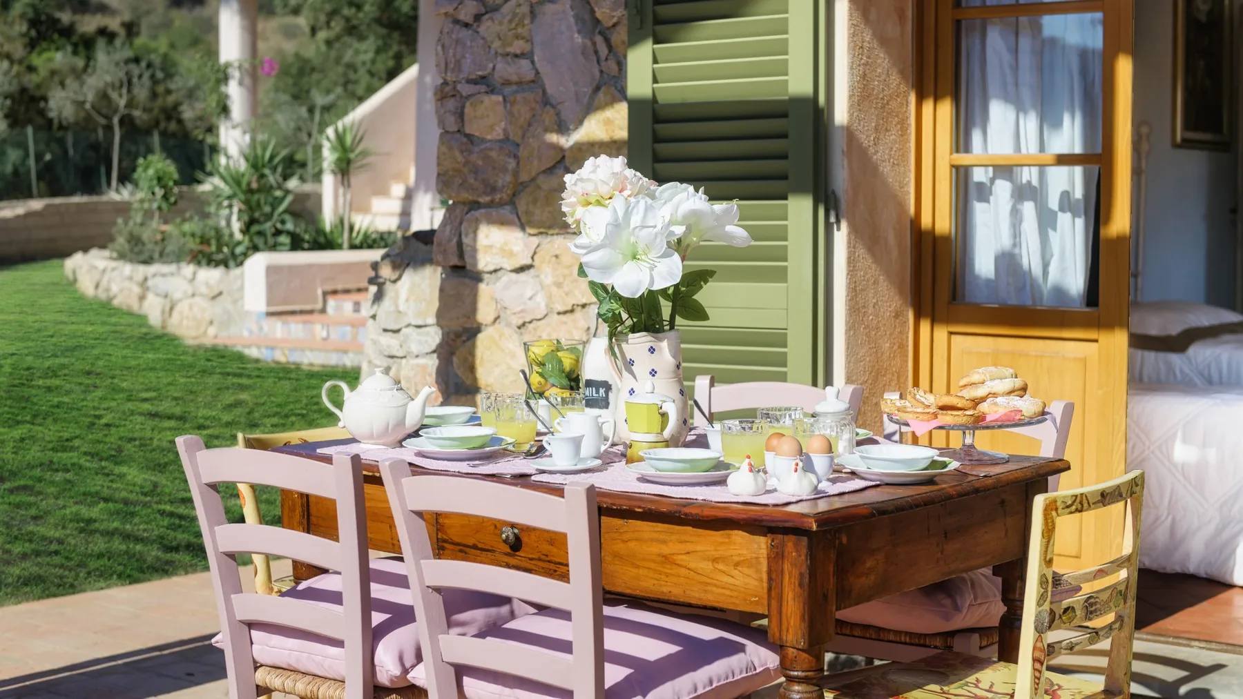 Una mesa de comedor al aire libre está puesta con platos y un jarrón de flores junto a una casa.