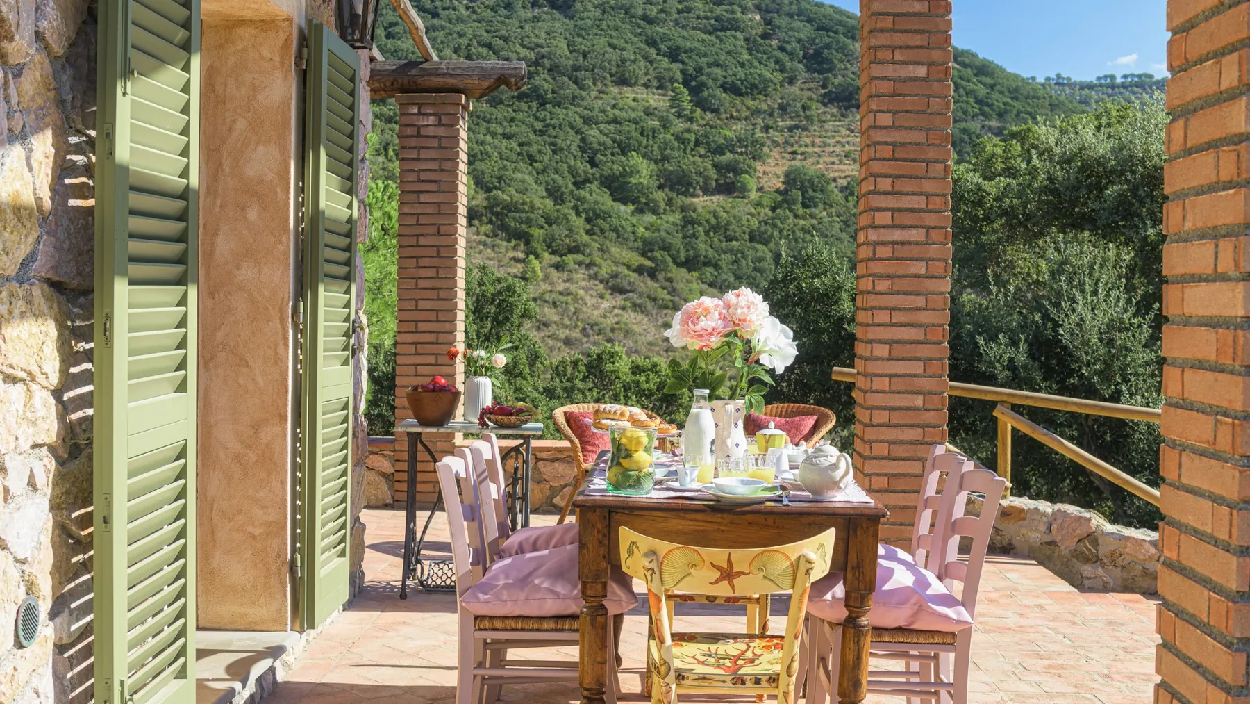 Una zona de comedor al aire libre, con mesa y sillas, da a una ladera verde.