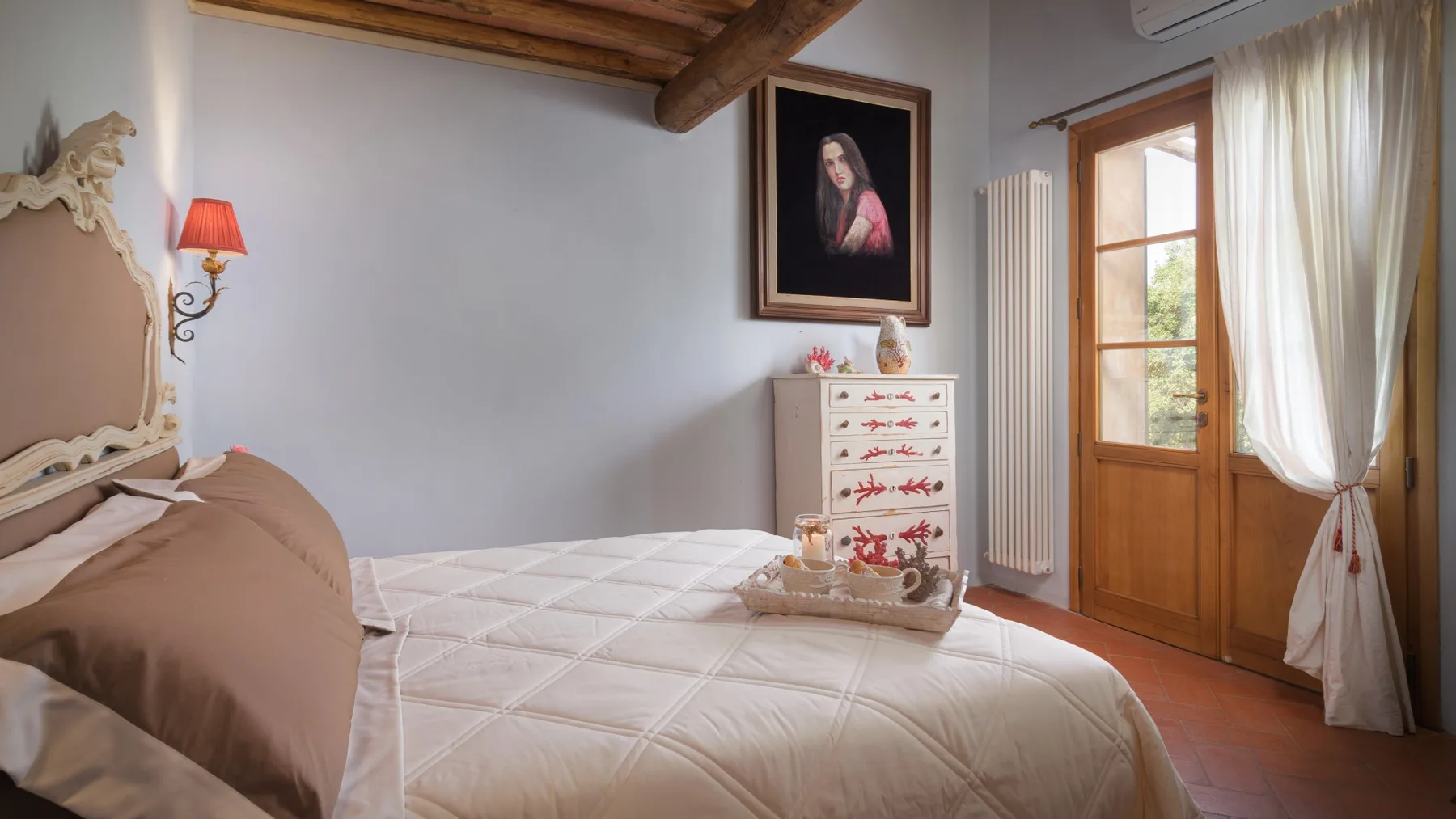 Un dormitorio con cama, cómoda y puerta de madera junto a una ventana con cortinas.
