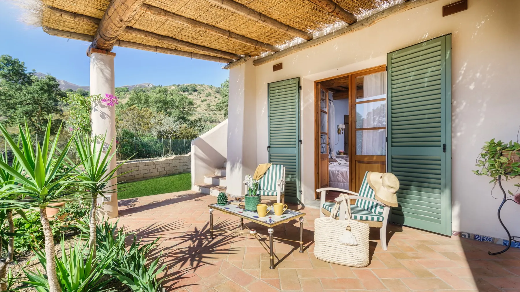 Un patio sombreado con asientos al aire libre y contraventanas verdes abiertas.